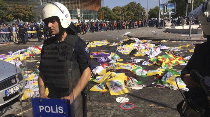 Bodies of victims are covered with flags and banners as a police officer secure the area after an explosion in Ankara, Turkey, Saturday, Oct. 10, 2015. Two bomb explosions apparently targeting a peace rally in Turkey's capital Ankara on Saturday has killed many people a news agency and witnesses said. The explosions occurred minutes apart near Ankara's train station as people gathered for the rally organized by the country's public sector workers' trade union. (AP Photo/Burhan Ozbilici)